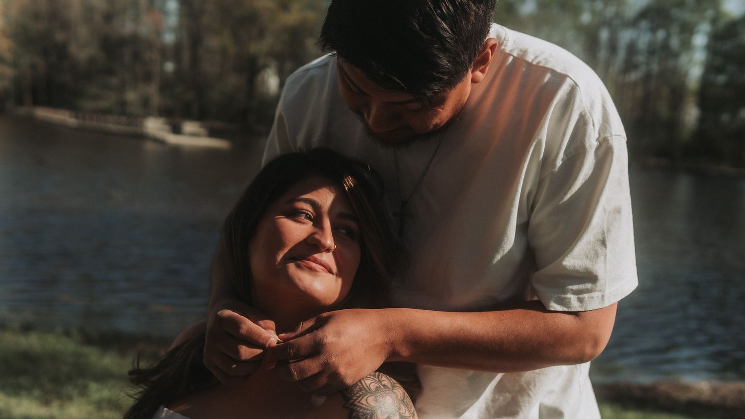 Loving couple embracing and laughing together outdoors near a sunlit lake.