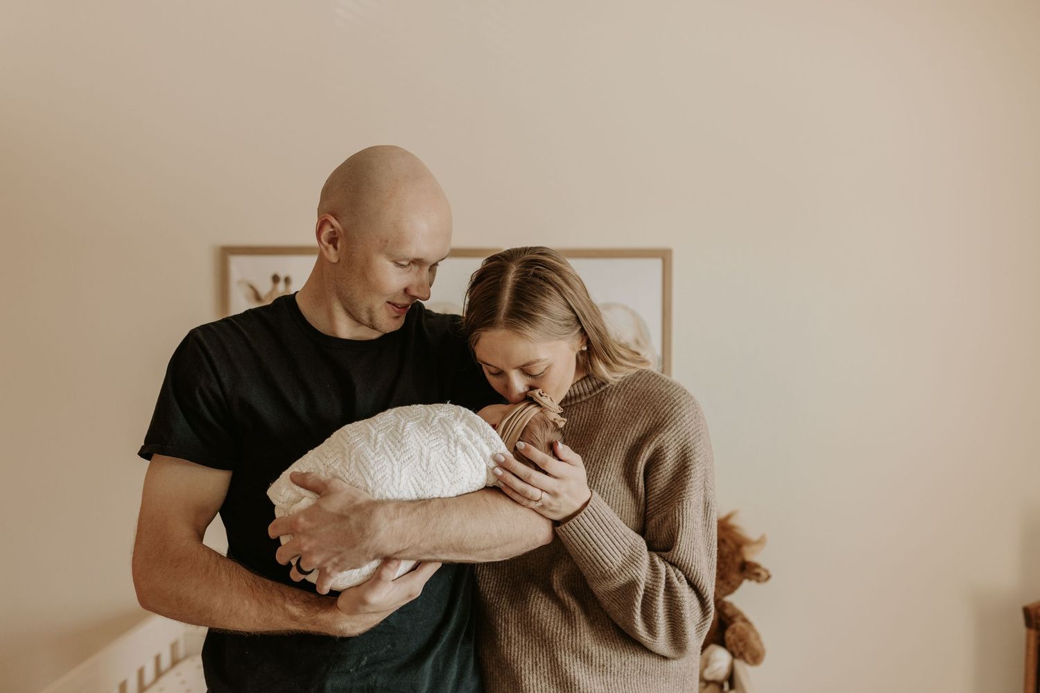 New parents tenderly holding their newborn baby together in a warmly lit nursery room.