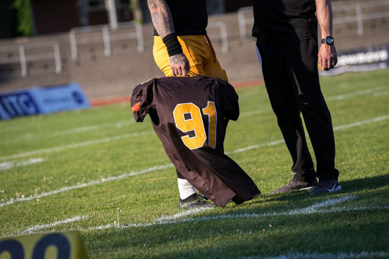 Football player #9 in black and gold uniform runs with the ball as defender #14 in green pursues during a game.