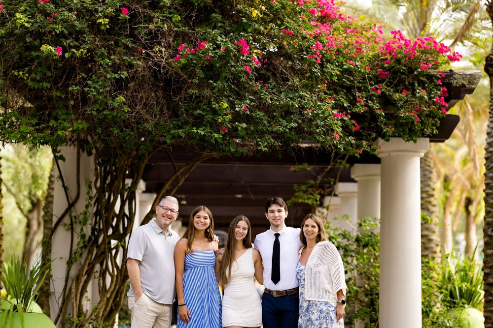 Family of five posing under a floral pergola with bougainvillea, dressed in formal attire outdoors.