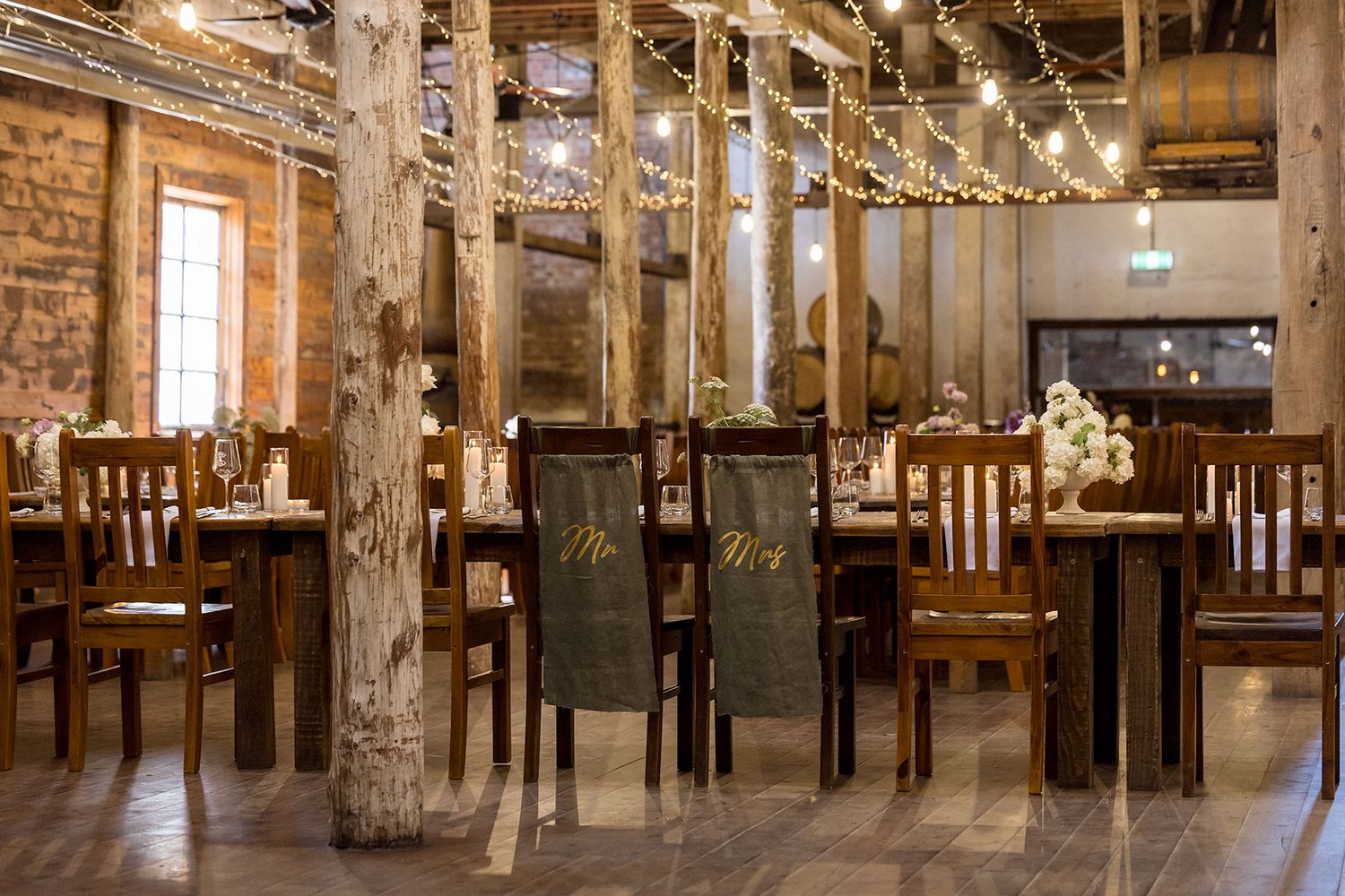 Rustic wooden interior with long communal dining tables set for a special wedding event under warm lighting at the Corowa Distilling Co..