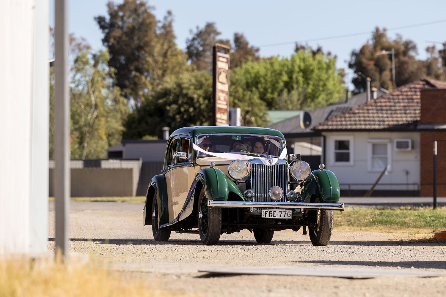 Vintage green classic car with chrome accents parked on a road with trees in the background.