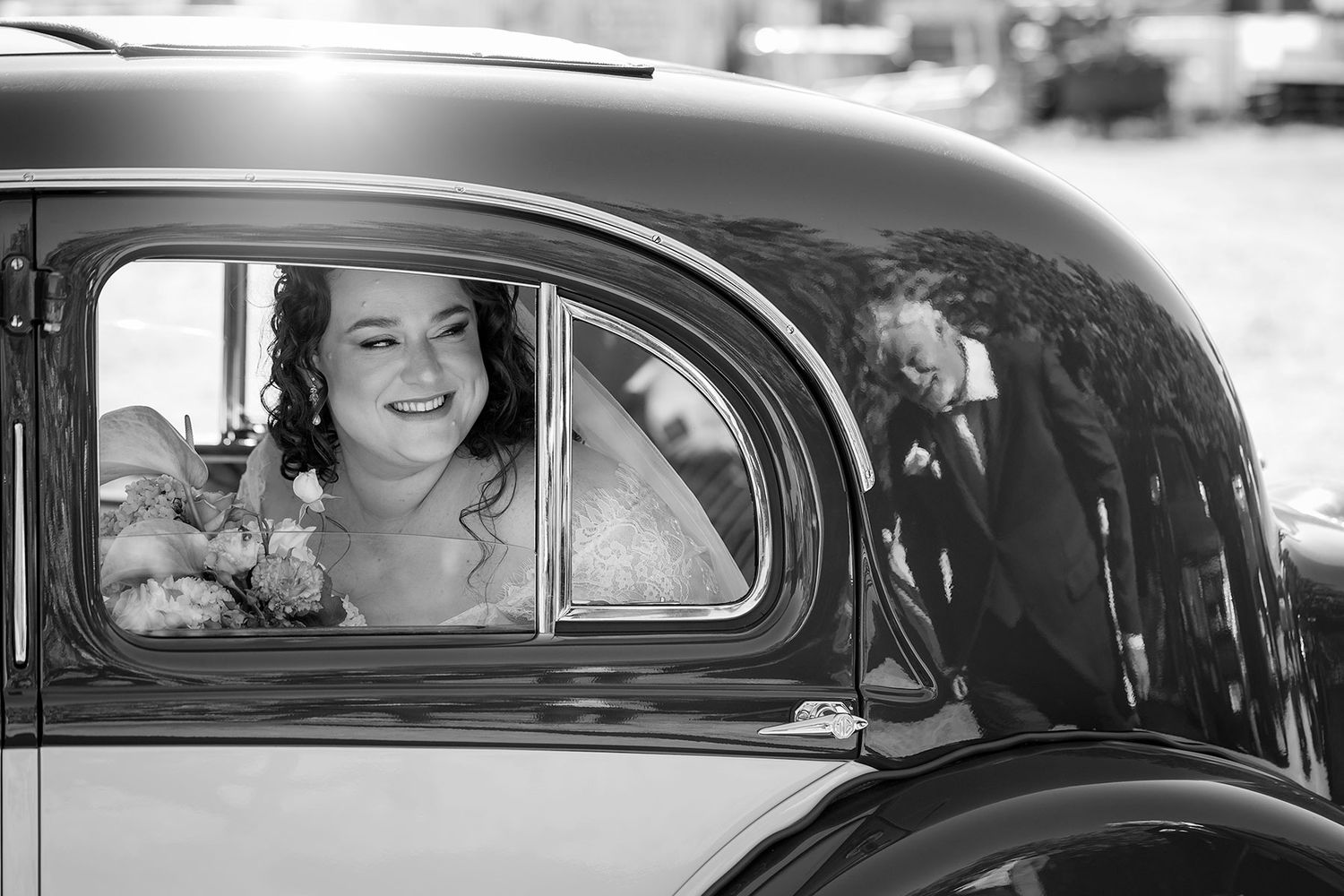 A vintage black and white photograph shows a Bride in a classic car with a reflection of her Dad in the paint at Corowa Distilling Co.
