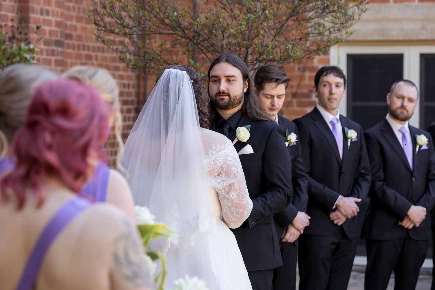 A wedding ceremony takes place outdoors against a red brick building on a sunny afternoon at the Corowa Distilling Co.