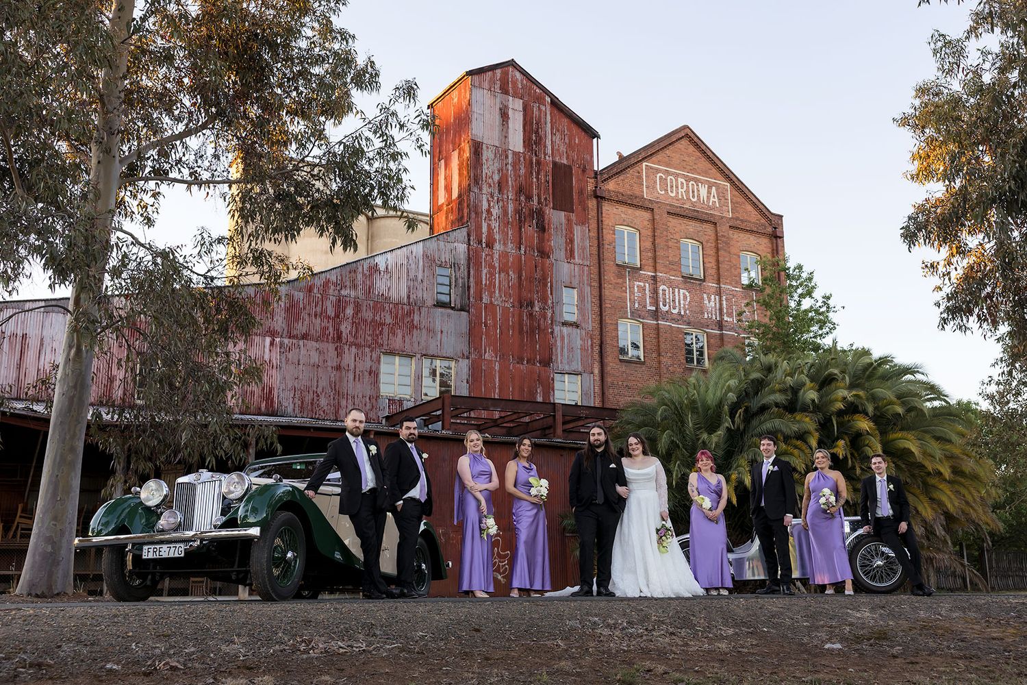 Wedding party gathers outside historic red brick building at sunset for outdoor photography session at the Corowa Distilling Co.