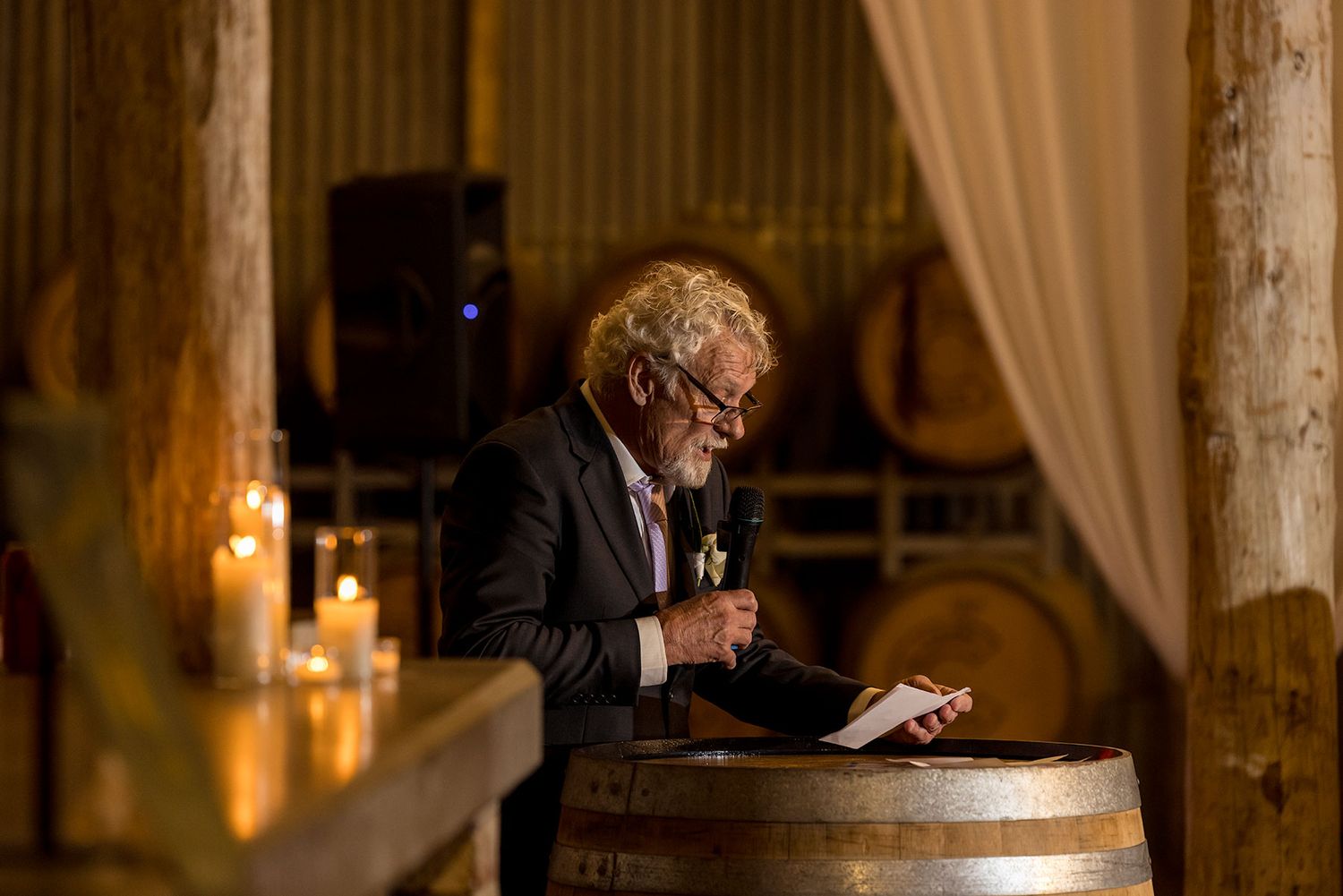 A Father of the Bride gives his speech leaning on a wooden wine barrel in a candlelit rustic venue at the Corowa Distilling Co.