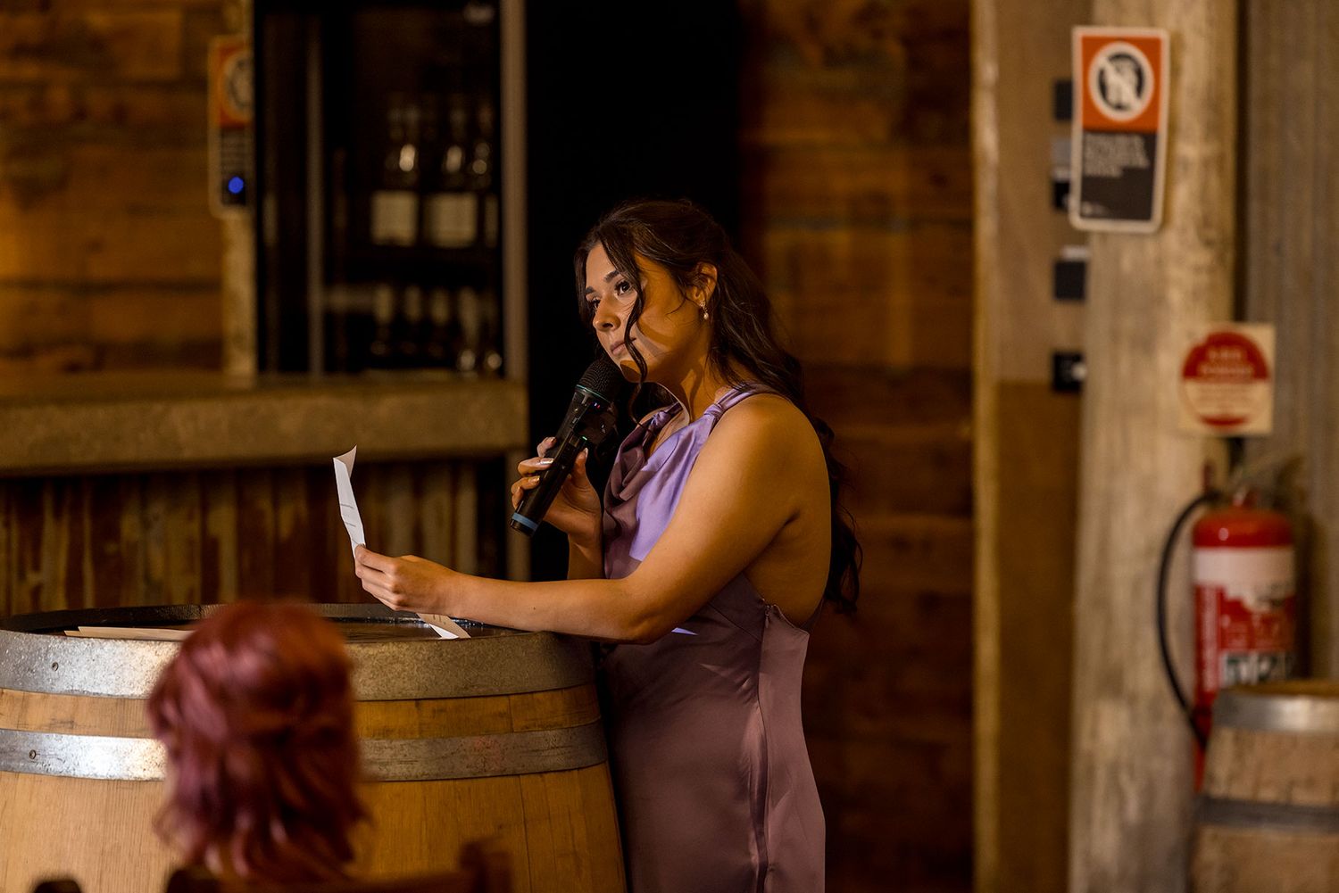 A Maid of Honour gives her speech leaning on a wooden wine barrel in a candlelit rustic venue at the Corowa Distilling Co.