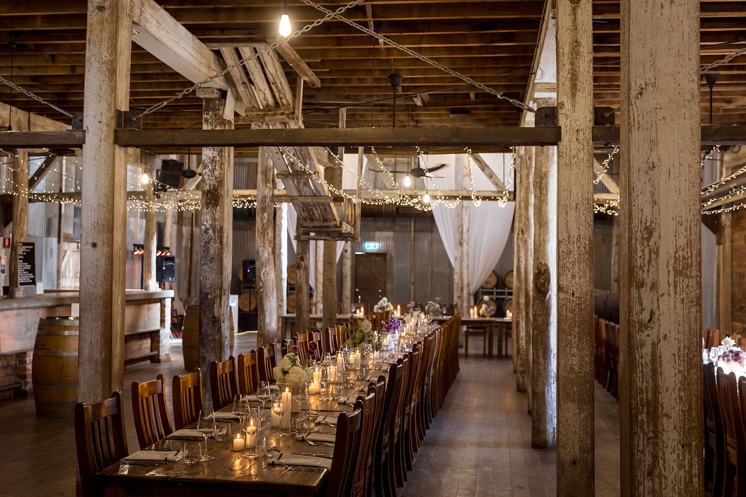 Rustic wooden interior with long communal dining tables set for a special wedding event under warm lighting at the Corowa Distilling Co..