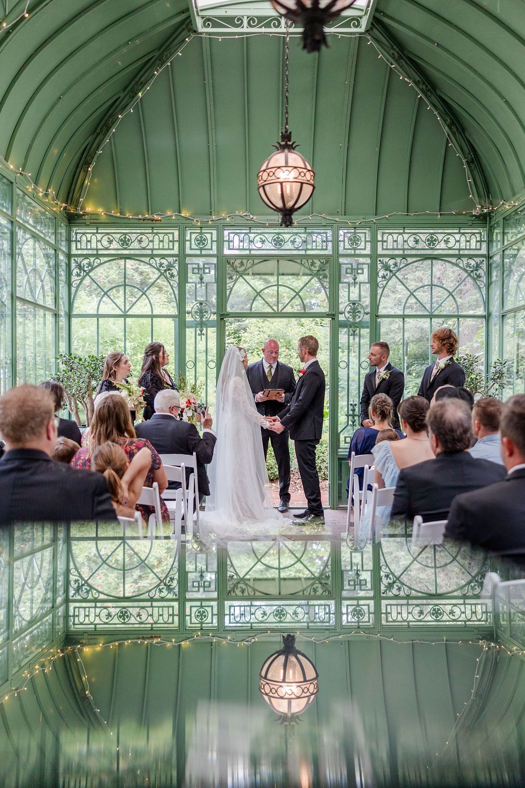 Wedding ceremony taking place in an elegant glass conservatory with green-tinted windows and ornate architectural details.