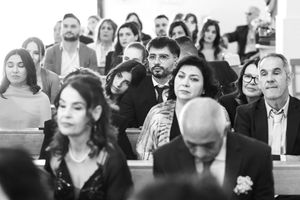 Wedding ceremony guests seated in church pews during an emotional moment.