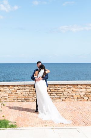 Romantic seaside wedding photos against a stone wall and blue ocean backdrop.