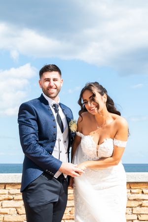 Seaside wedding photos with couple posing against stone wall under blue sky.
