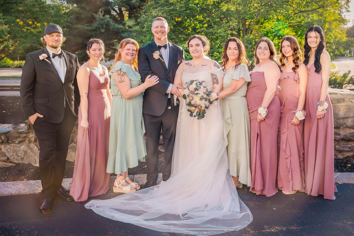 Wedding party in pink and sage green dresses poses together outdoors during sunset ceremony.