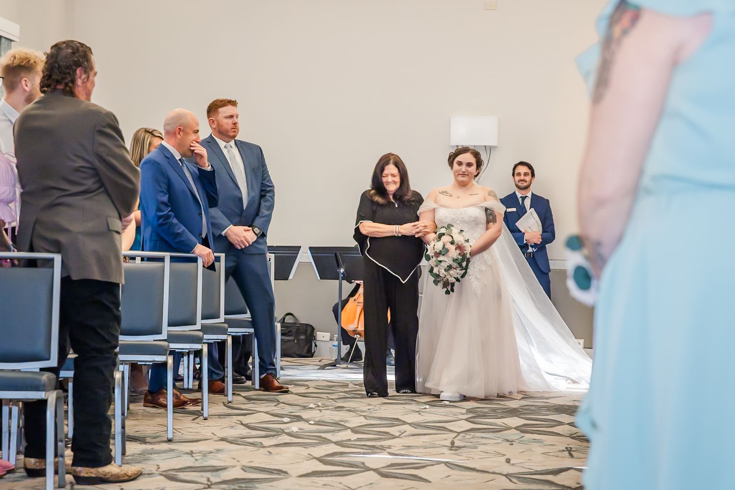 Wedding guests dance and celebrate on a patterned stone floor during an indoor reception.