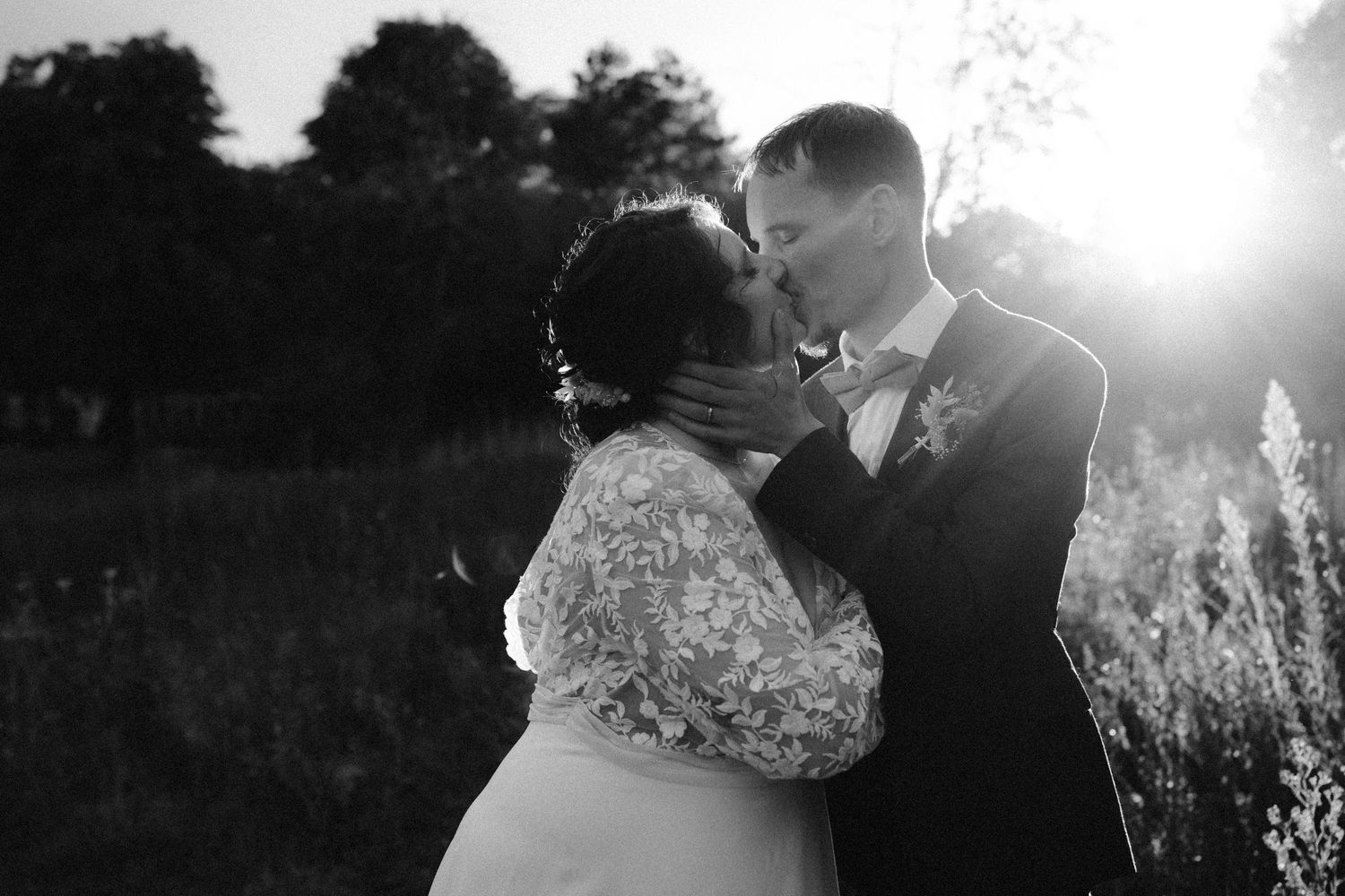 A romantic black and white wedding photograph showing a tender embrace in a natural outdoor setting.