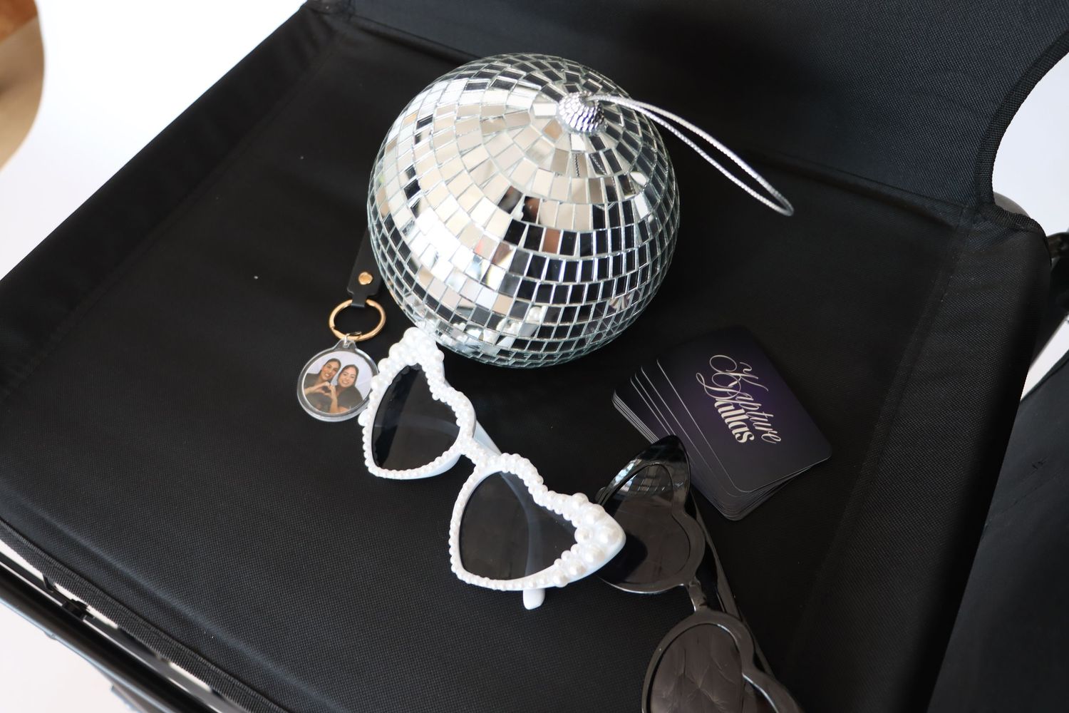 Disco ball, heart sunglasses, ring, and Kristure Dallas cards arranged on a black surface.