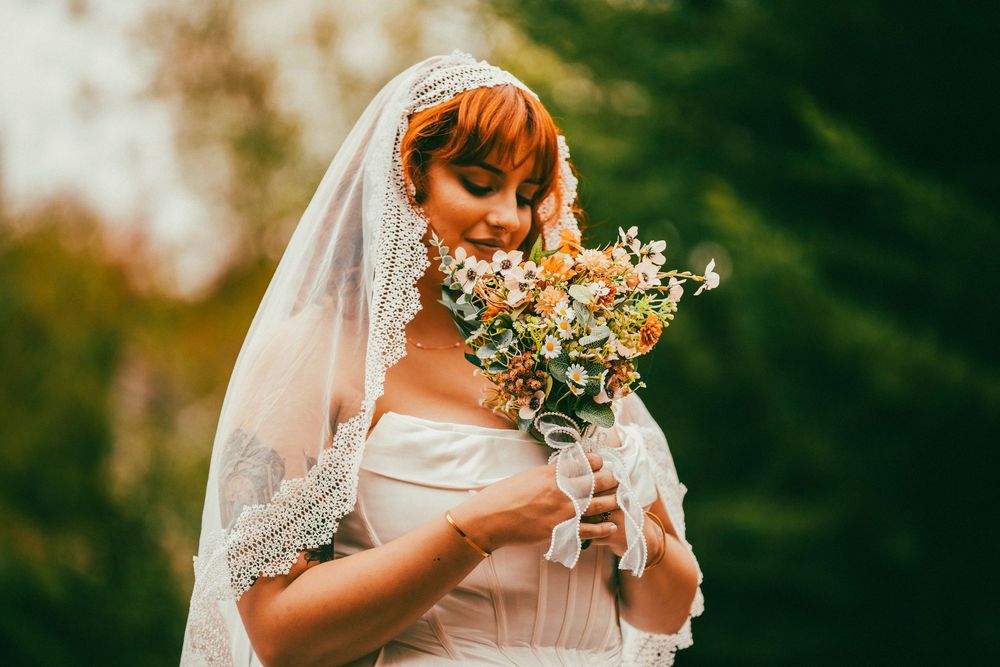 Bride holds delicate floral bouquet against autumn foliage backdrop.