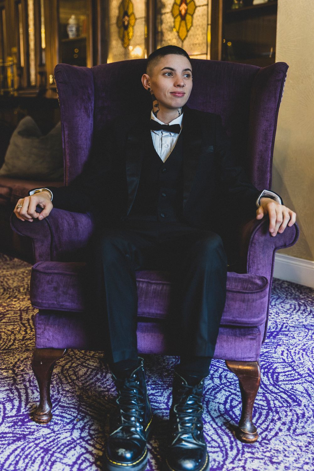 Black dress shoes and formal attire shown against a purple velvet chair and patterned carpet.