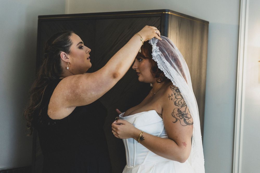 A wedding preparation scene shows final adjustments being made to a white veil and dress.