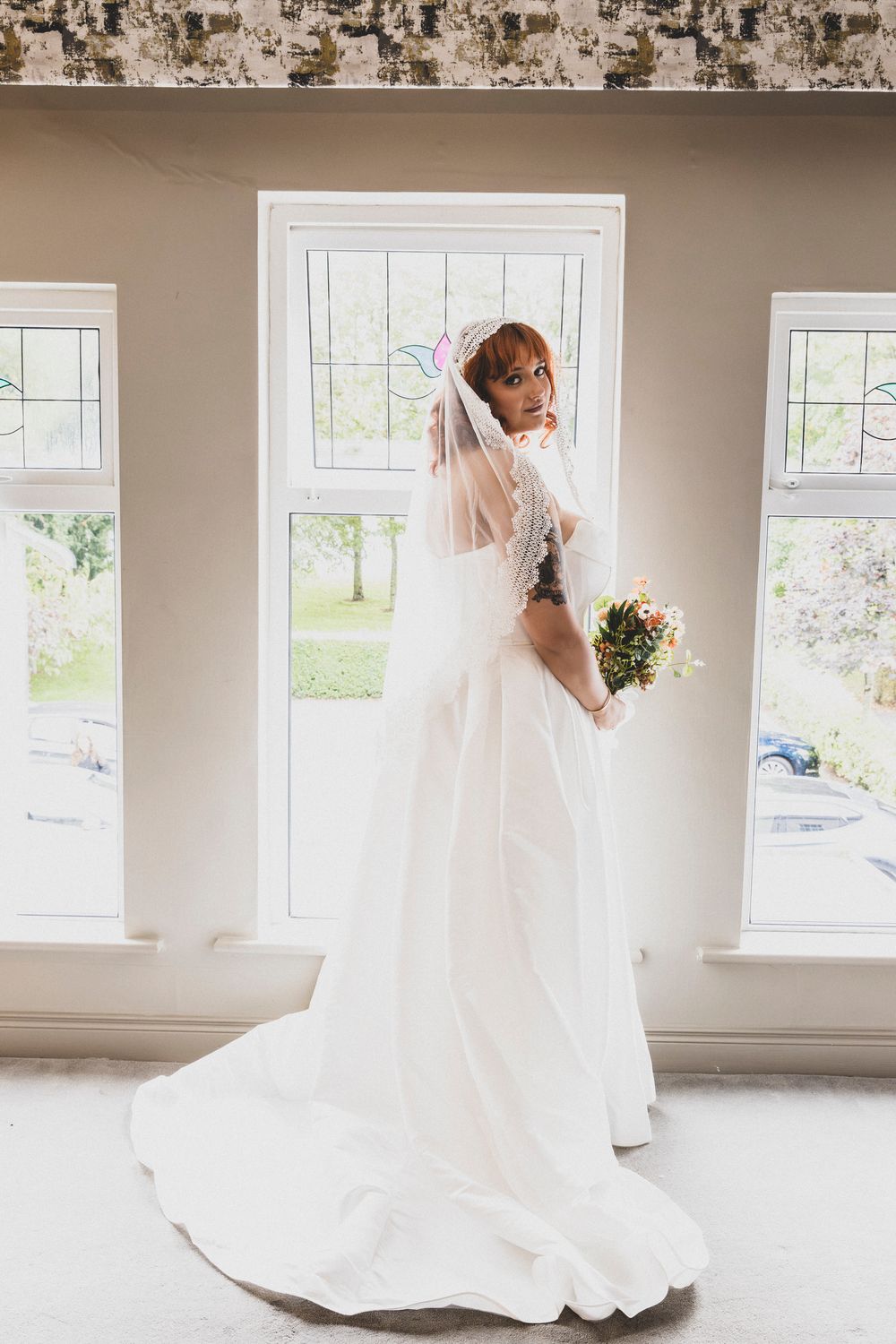 A bride in a classic white ballgown spins elegantly in a bright room with multiple windows.