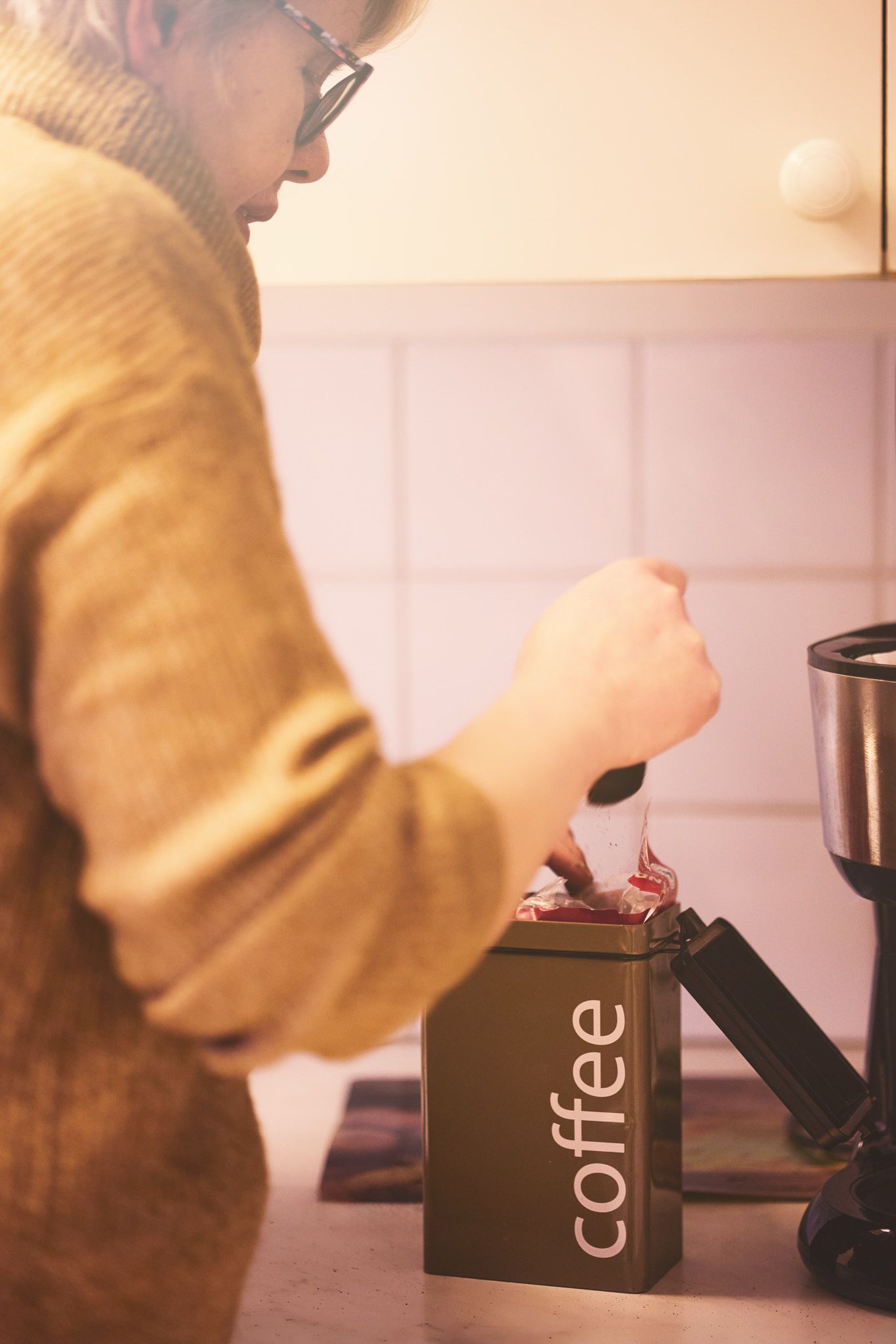 Person in yellow sweater preparing coffee with a modern coffee maker in warm lighting.