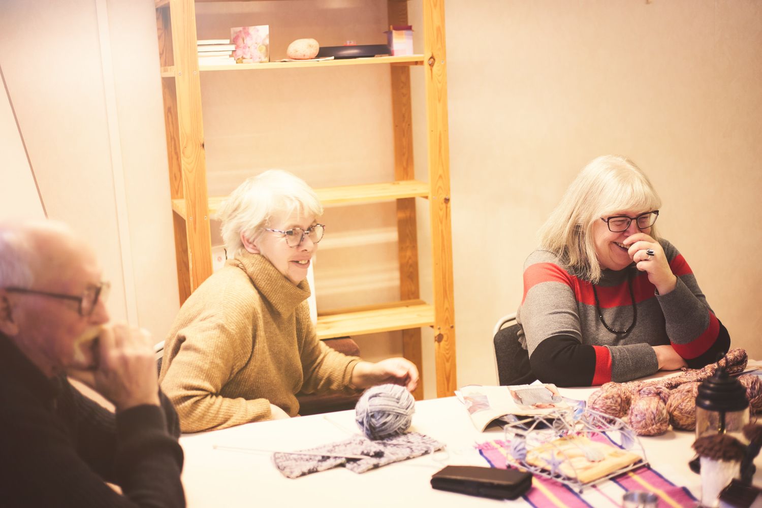 Students working together at tables in a classroom setting with wooden shelving visible in the background.