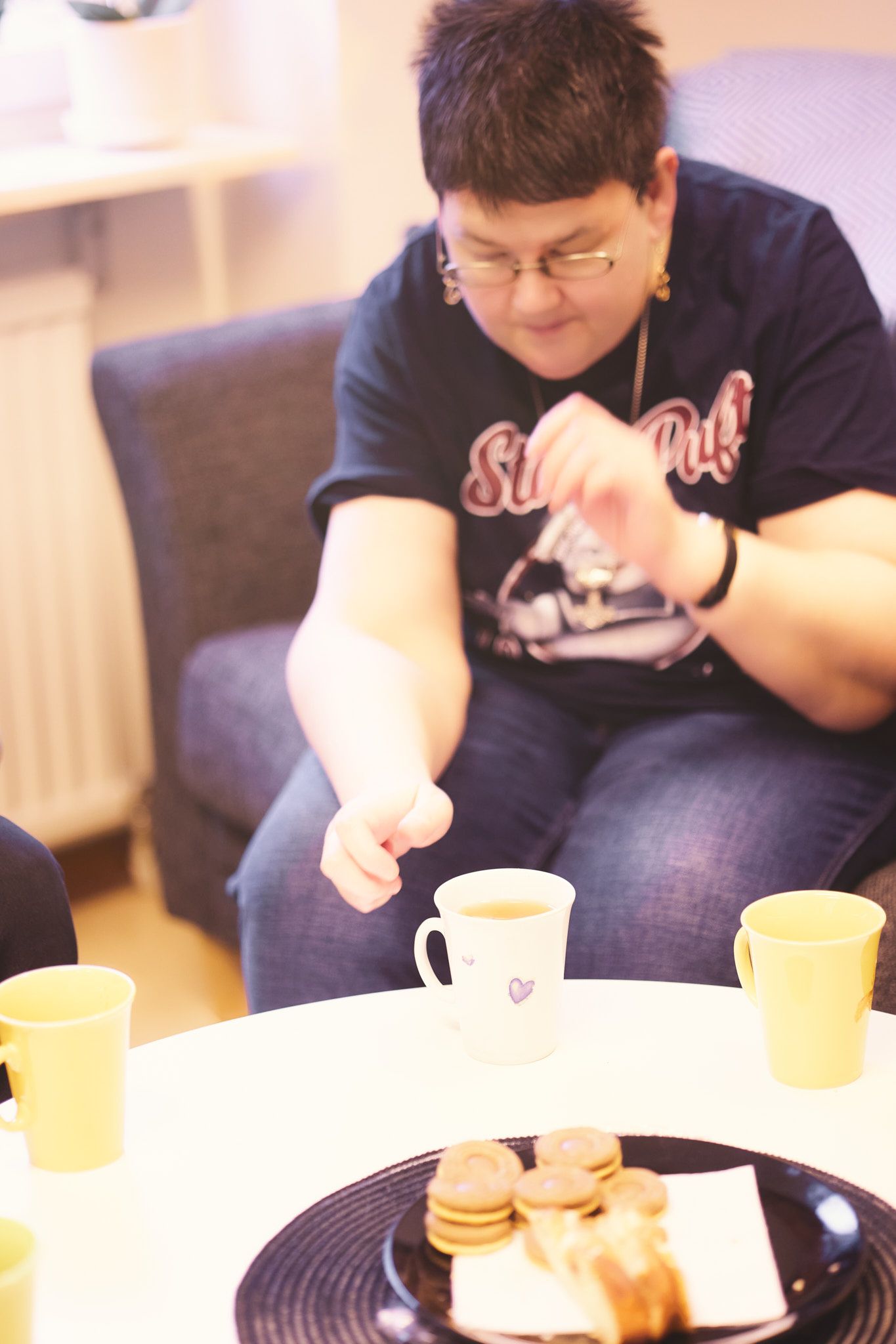 Person in blue shirt sits at table with coffee mug and snacks in soft indoor lighting.