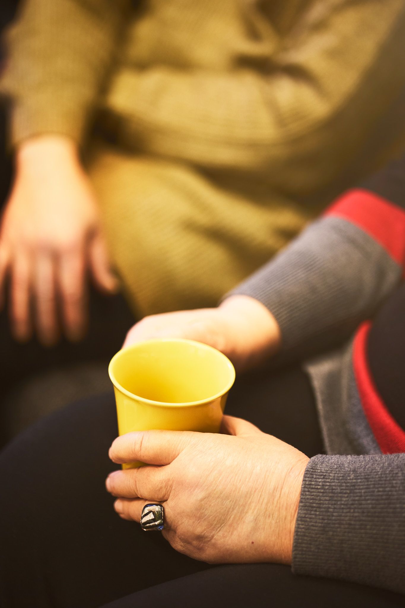 Close-up view of hands holding a small yellow ceramic cup against a dark background.