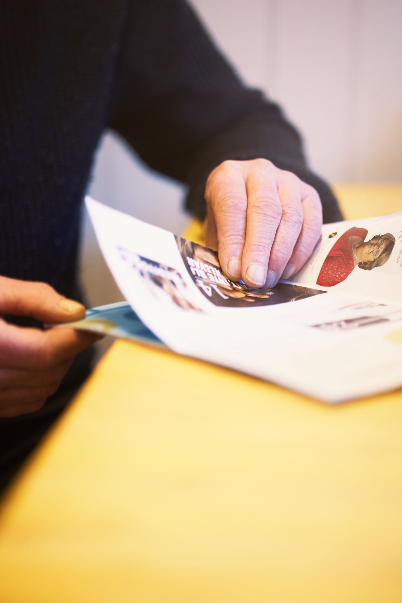 Hands sorting through papers or documents on a yellow surface in natural lighting.