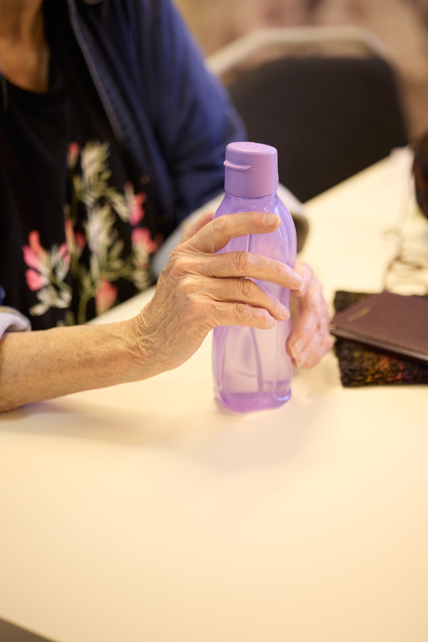 Hands holding a purple reusable water bottle against a white surface.
