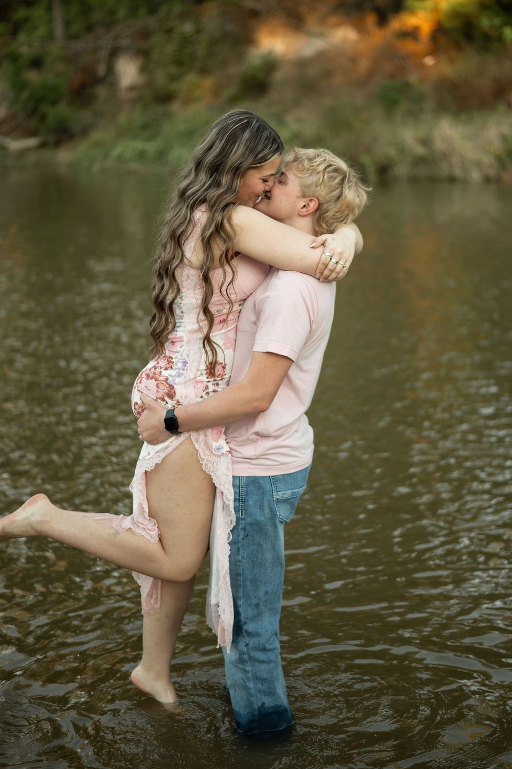 Romantic couple embracing in shallow water at sunset with autumn colors reflecting in the lake.