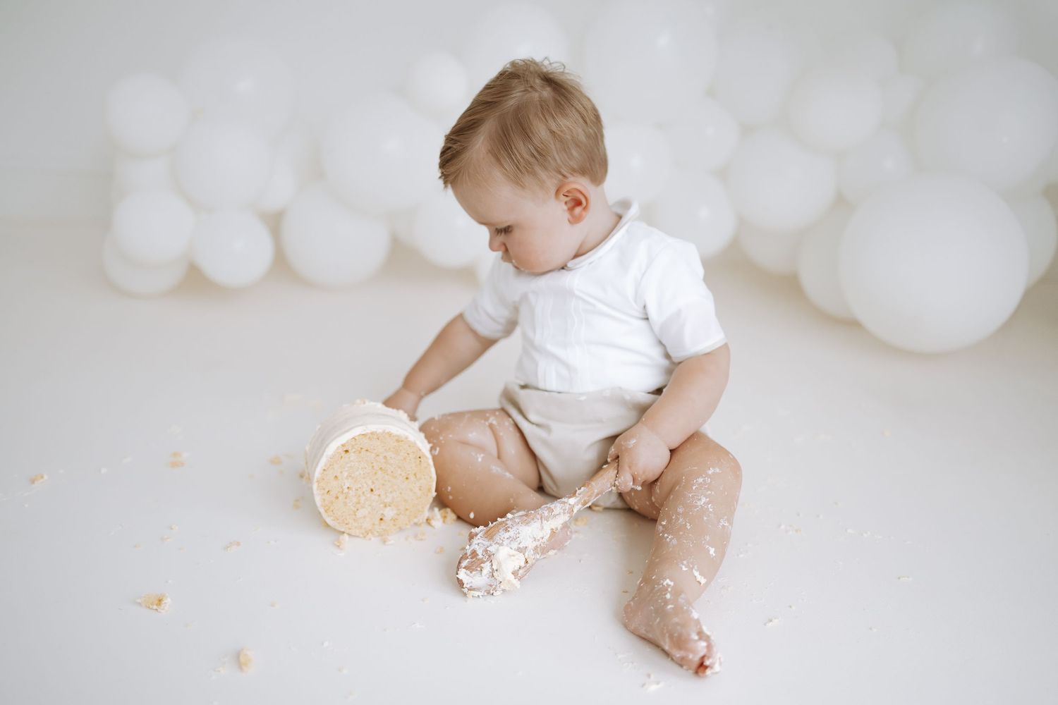 A small child in a white shirt sits on a white background playing with fluffy cotton-like material.