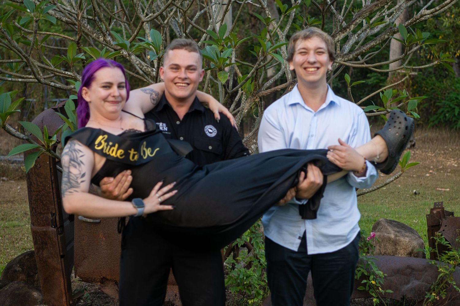 Group of people posing and smiling together outdoors in a garden setting with trees in the background.