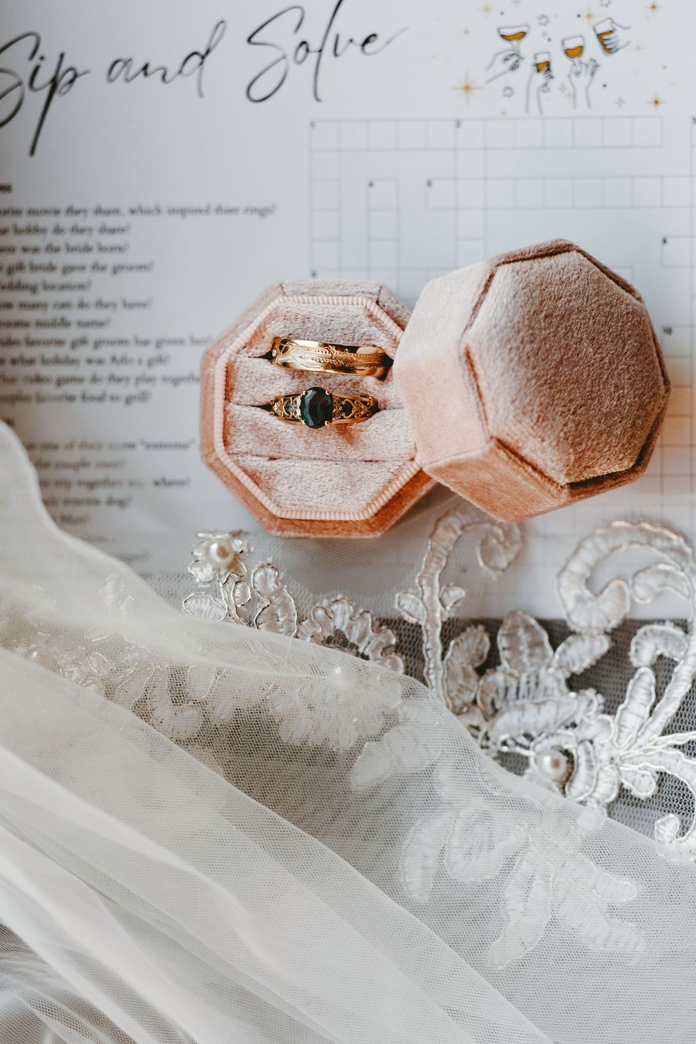 Gold wedding rings with dark gemstone displayed in pink velvet octagonal ring box on lace bridal veil.