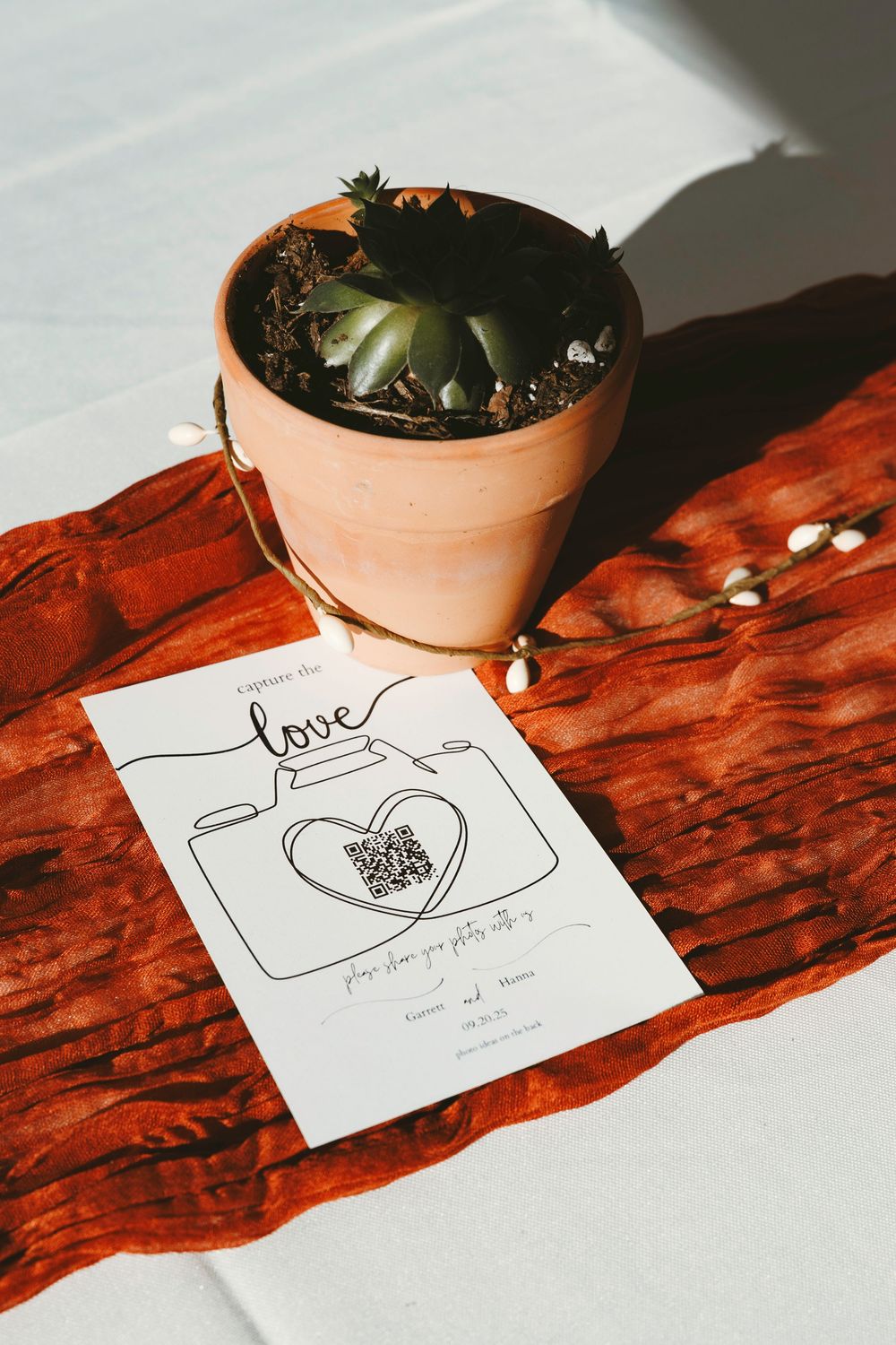 Wedding photo sharing card with QR code beside terracotta succulent pot on rustic red wood slice.