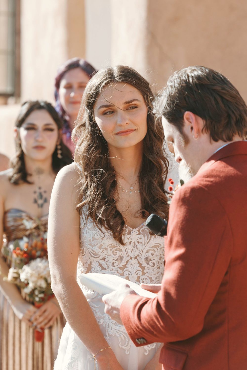 Bride in lace wedding dress gazes at groom during outdoor wedding ceremony vows.
