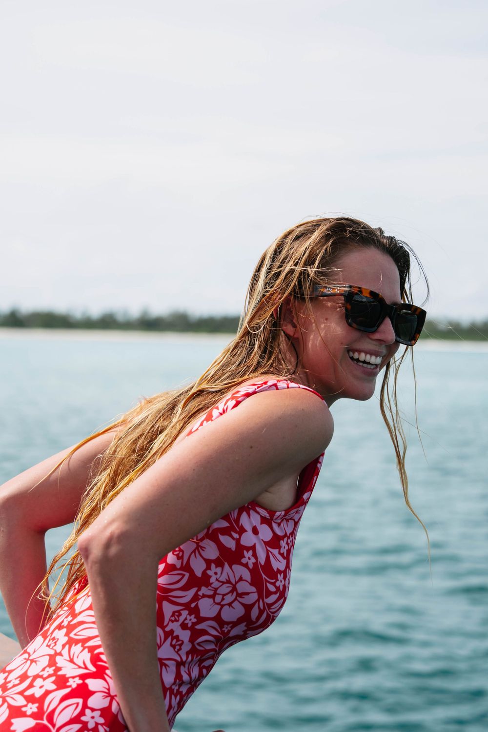 A sequence of someone in a red and white floral swimsuit leaning over the edge of a boat on tropical waters.
