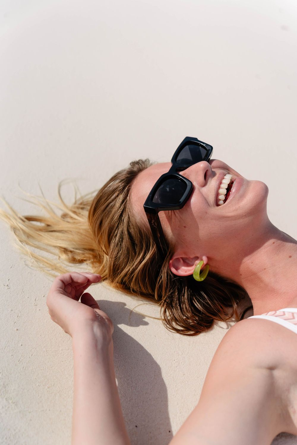 A person with blonde hair and a black blindfold reclines against a white wall in a dramatic pose.
