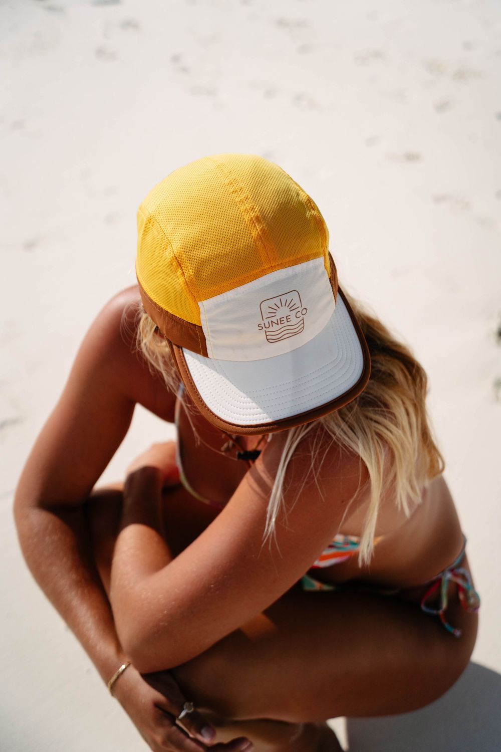 A person wearing a yellow baseball cap sits in a contemplative pose against a light background.