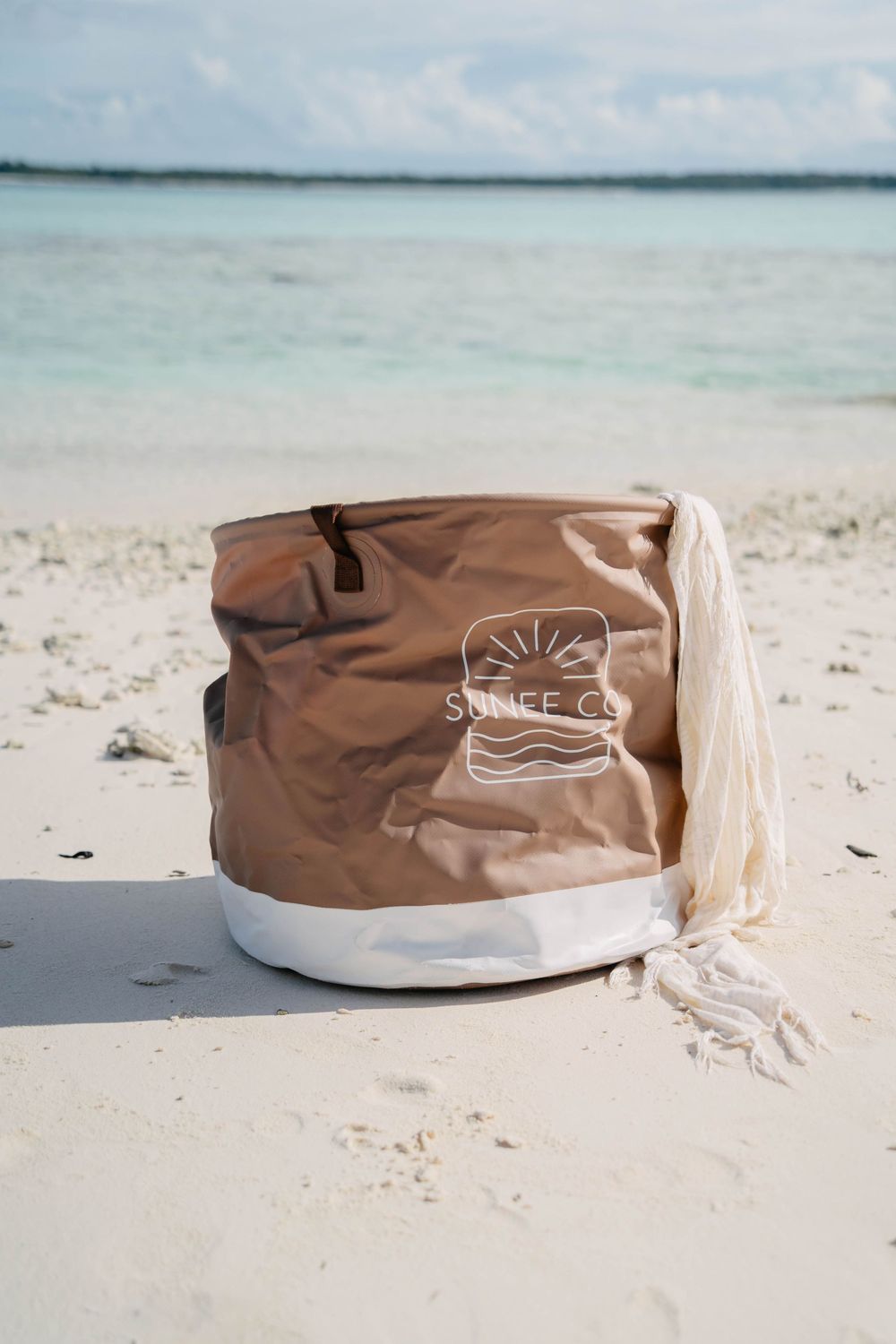 A brown and beige beach chair bag sits on white sandy beach with turquoise ocean waters in the background.