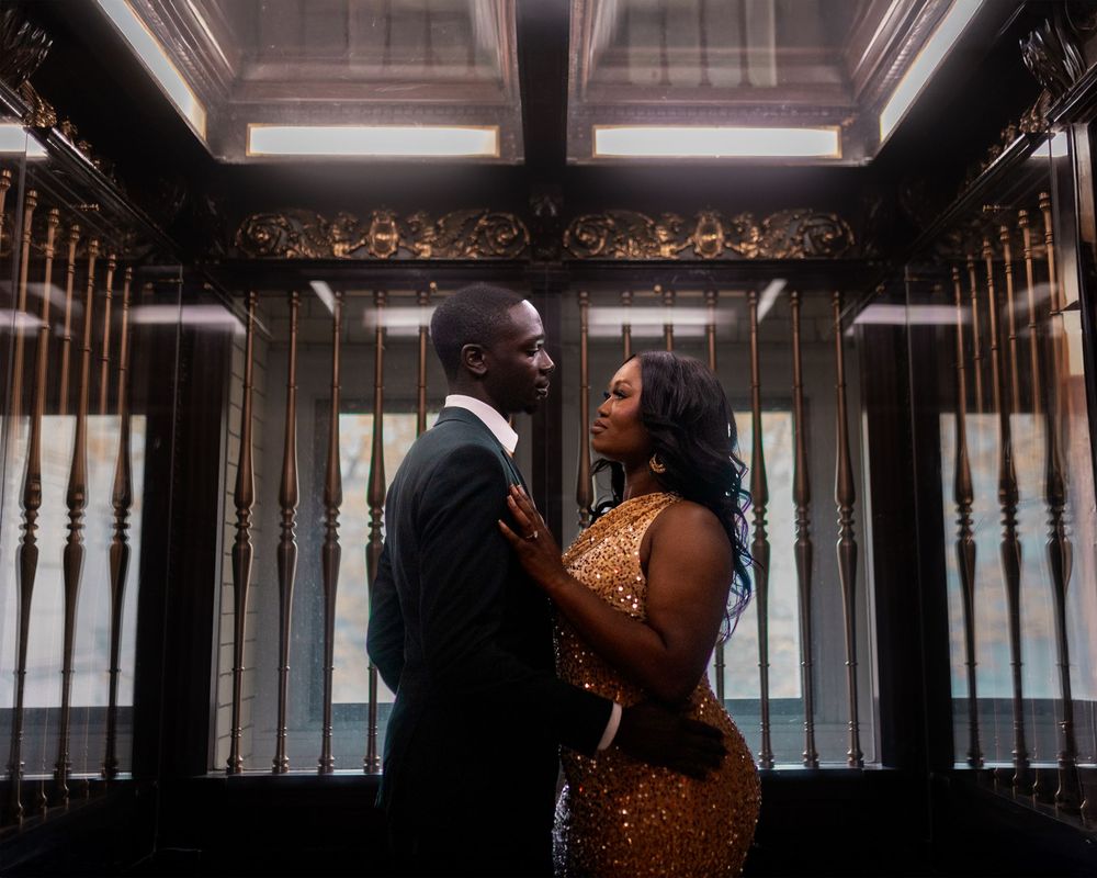 A couple shares an intimate moment in an elegant hallway with ornate details and warm lighting.
