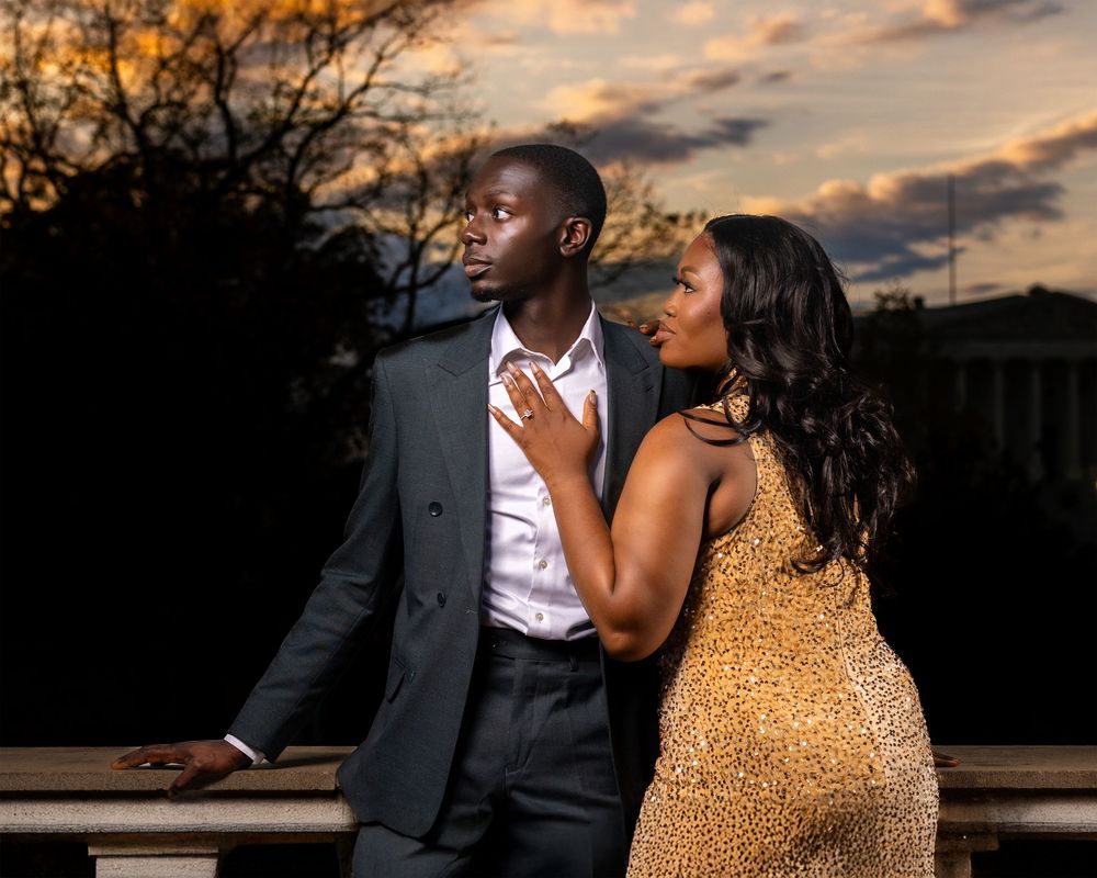 A romantic couple poses at sunset, with one wearing a gold sequin dress and the other in a dark suit and white shirt.