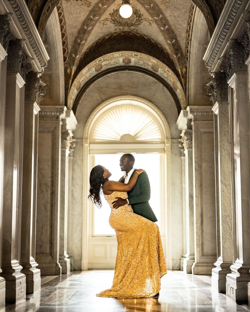 A romantic couple poses in an elegant columned hallway with arched architecture and a flowing yellow dress.