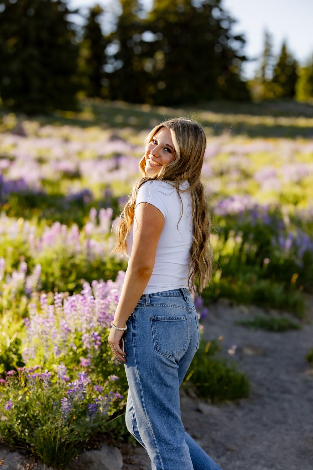 Summer portrait among purple wildflowers with casual denim and white top outfit.