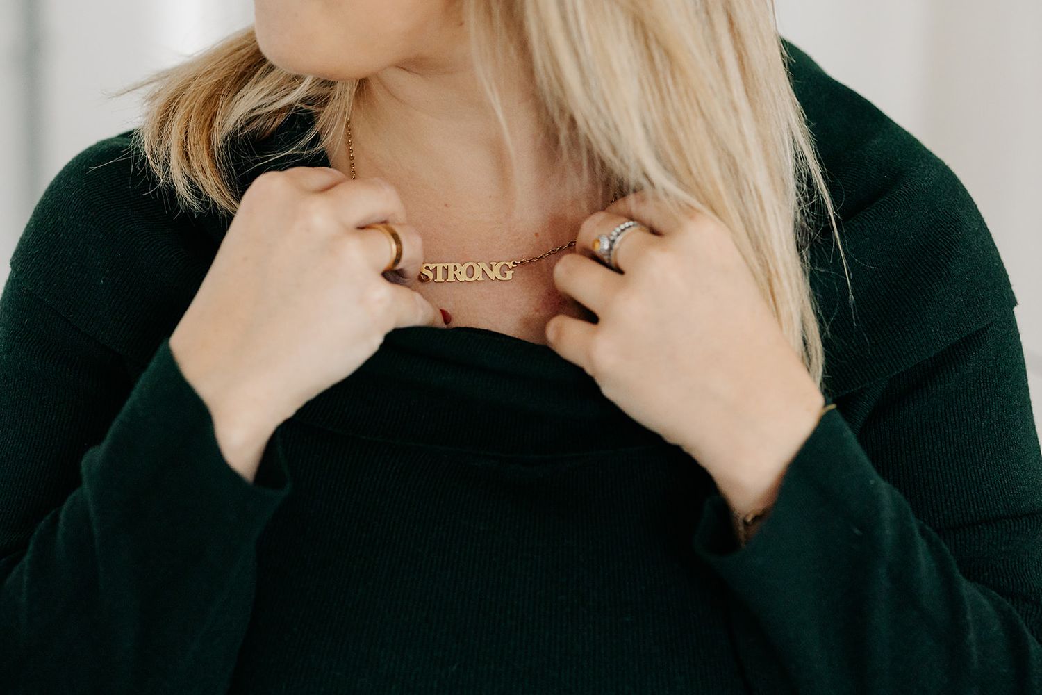 A person wearing a black turtleneck sweater poses in a series of four close-up shots with different expressions. strong necklace