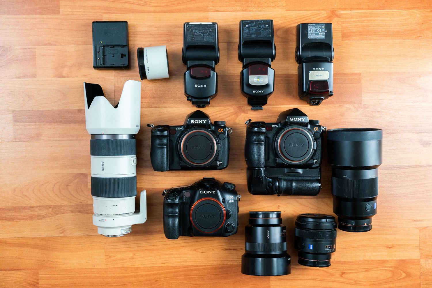 Professional camera equipment including multiple camera bodies, lenses, and flash units arranged on a wooden surface.