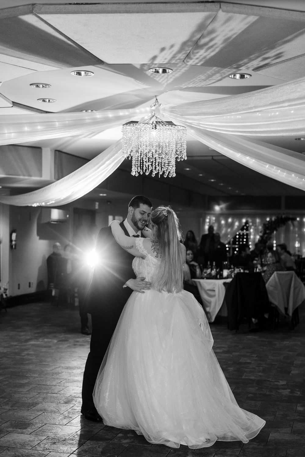 A romantic first dance at a wedding reception under elegant crystal chandeliers and draped fabric ceiling decor.