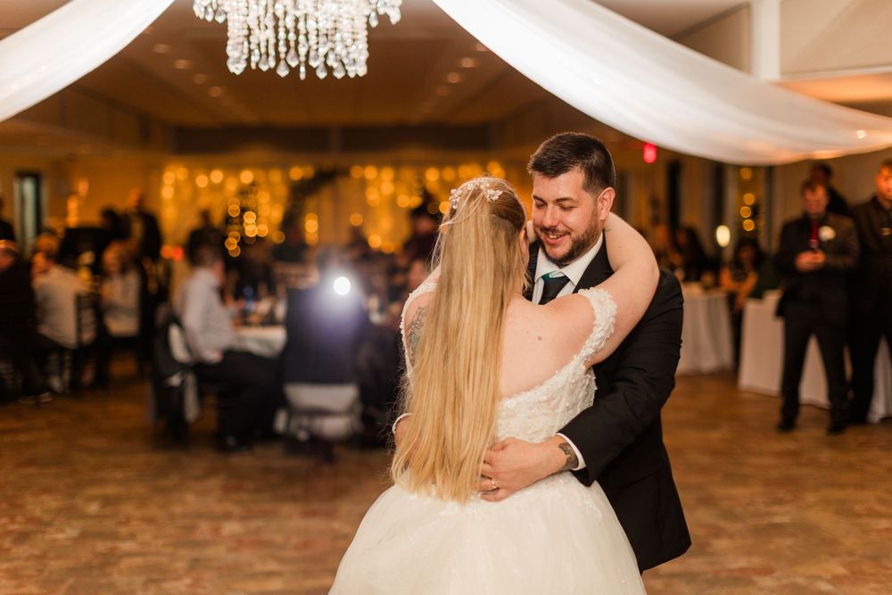 Romantic first dance at a wedding reception with white fabric draping and elegant chandelier lighting.