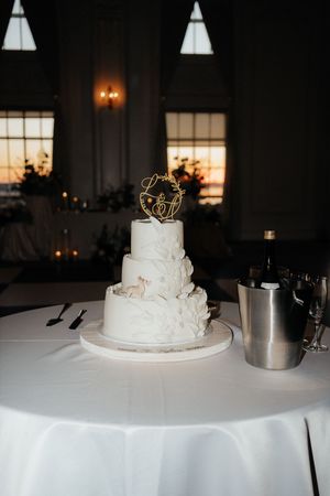 A white wedding cake with delicate decorations sits elegantly on a round table with a white tablecloth.