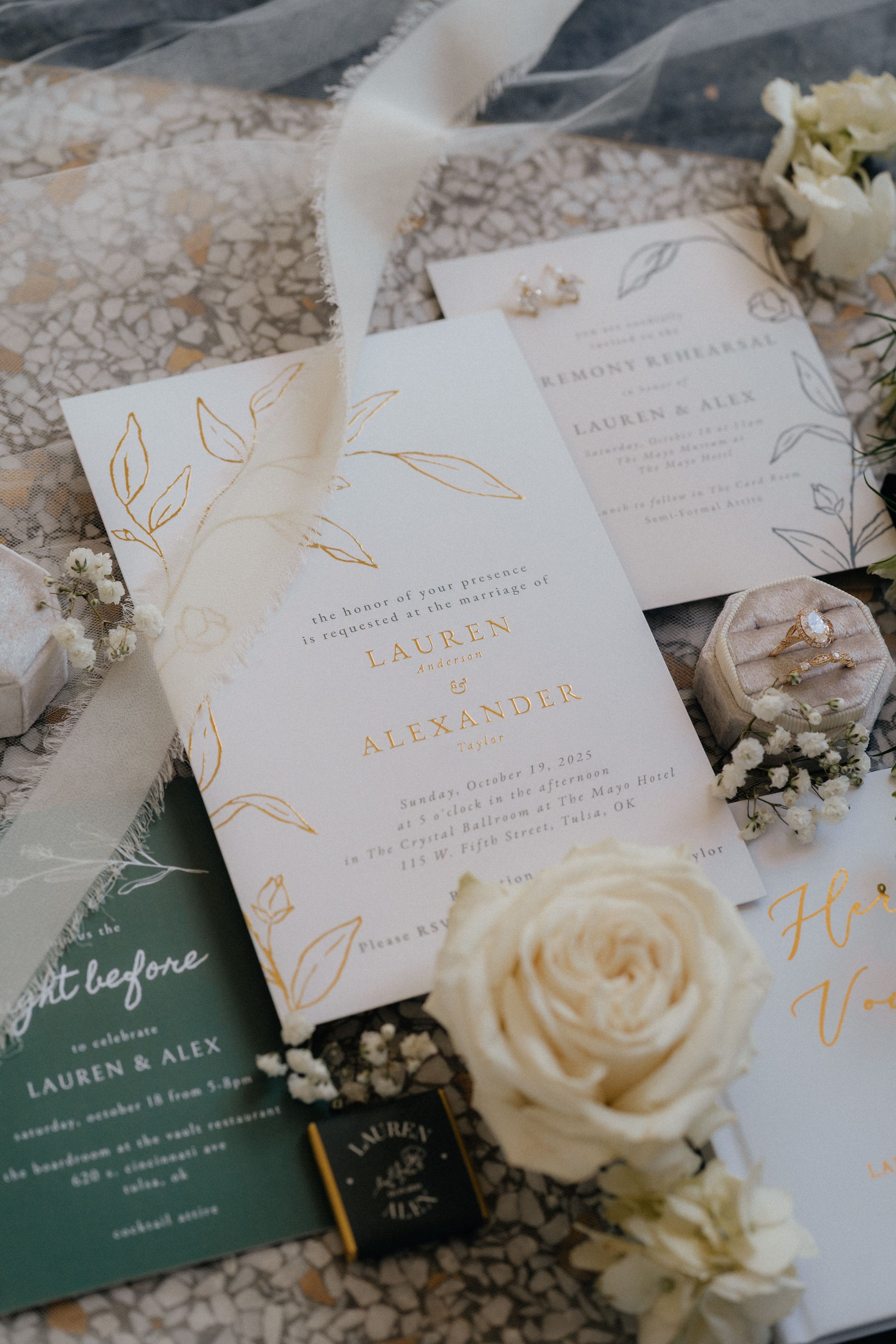 Elegant wedding invitations with gold calligraphy and white roses displayed on a textured surface.